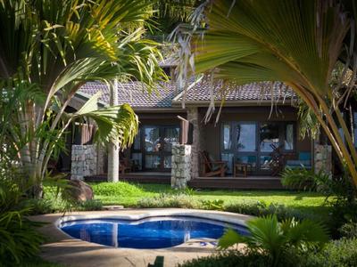 Maison confortable avec jardin et petite piscine entourée de plantes tropicales.