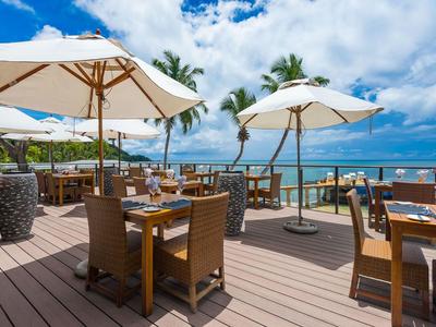Restaurant en plein air avec sol en bois, parasols blancs et vue sur la mer par ciel dégagé