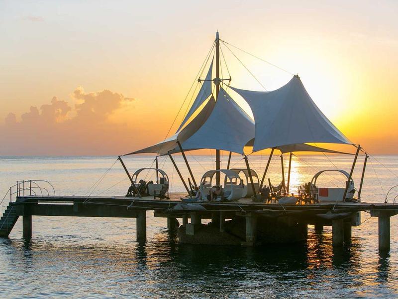 Un pavillon avec un toit en toile de voile sur une jetée au coucher du soleil au-dessus de l'eau.