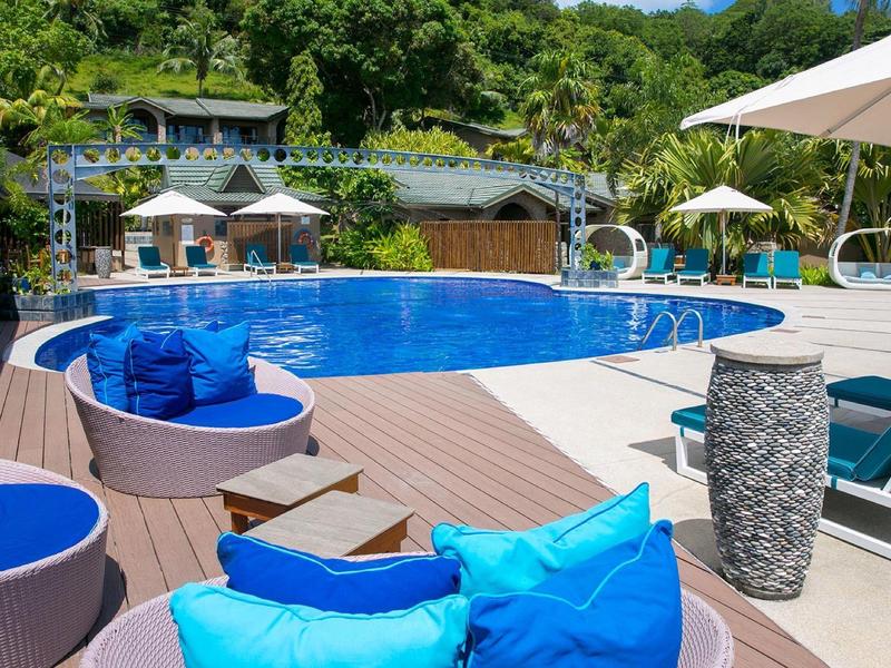 Espace piscine extérieur moderne avec coussins bleus et parasols, entouré de verdure.