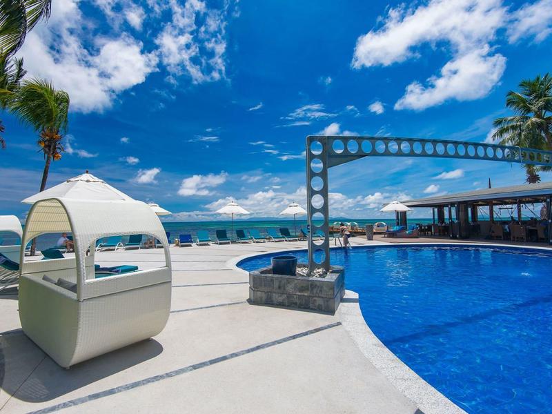 Espace piscine moderne avec vue sur la mer et sièges lounge sous un ciel bleu.