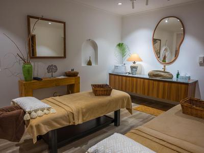 Una stanza spa accogliente con due lettini da massaggio, specchi e luce calda.