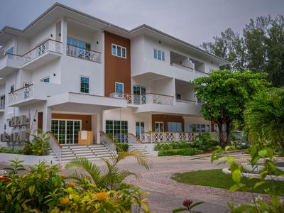 Edificio moderno di un hotel a tre piani con balconi e giardino ben curato sotto un cielo nuvoloso.