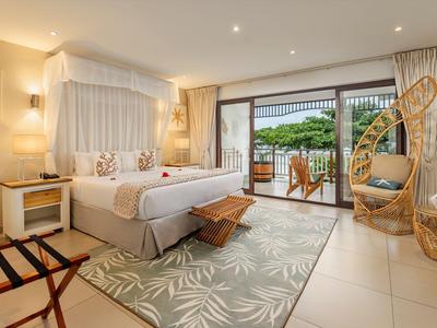 Helles Hotelzimmer mit großem Bett, Hängesessel und Terrasse mit Gartenblick.