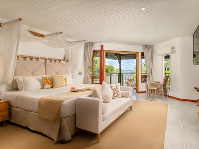 Helles Hotelzimmer mit großem Bett, Sofa, Balkon mit Meerblick und modernem Interieur.