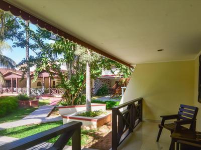 Balcon avec des chaises donnant sur un jardin et des maisons dans un cadre tropical.