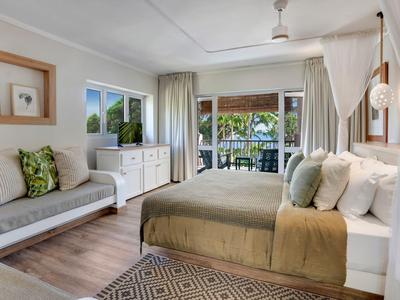 Hell eingerichtetes Schlafzimmer mit großem Bett, Sofa und Blick auf Balkon und Meer.