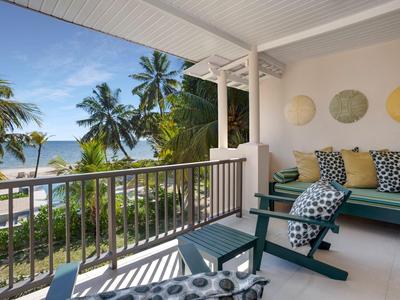 Balkon mit Sitzmöbeln, Blick auf Palmen und Meer bei sonnigem Wetter.