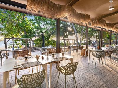 Offenes Restaurant mit Holzboden, modernem Mobiliar und Blick auf Garten und Himmel.