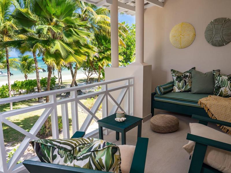 Balkon z zielonym umeblowaniem i widokiem na palmy i morze pod jasnym niebem
