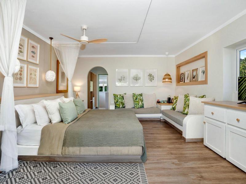 Jasna sypialnia z dużym łóżkiem, miejscem do siedzenia i neutralną dekoracją.