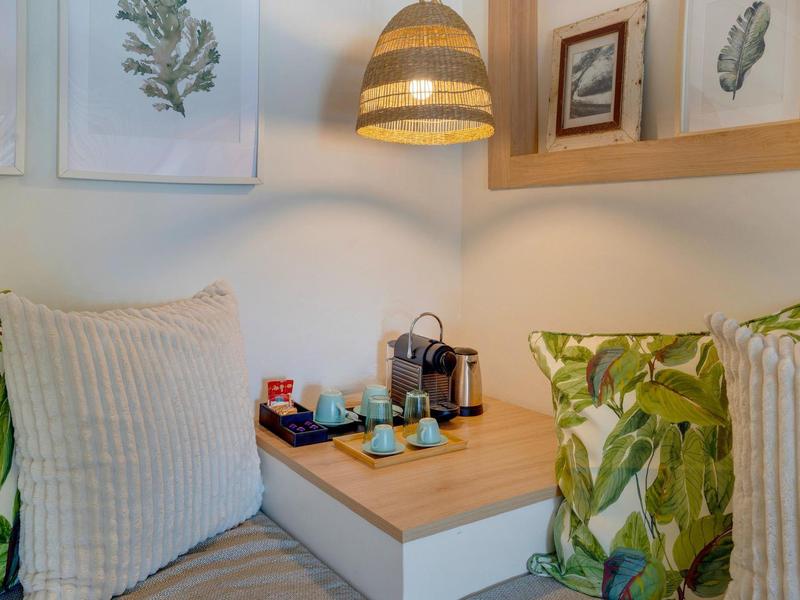 Przytulny kącik do siedzenia z poduszkami w liście, stacja kawowa i obrazami na ścianie, ciepłe światło.