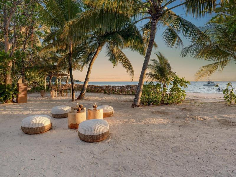 Drewniane miejsca do siedzenia z poduszkami na plaży pod palmami o zachodzie słońca.