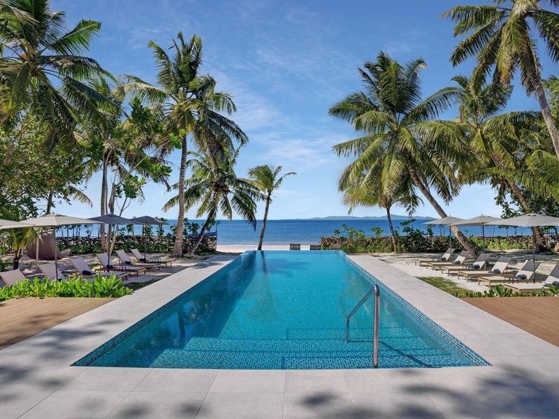 Długi basen otoczony palmami z widokiem na morze i parasole