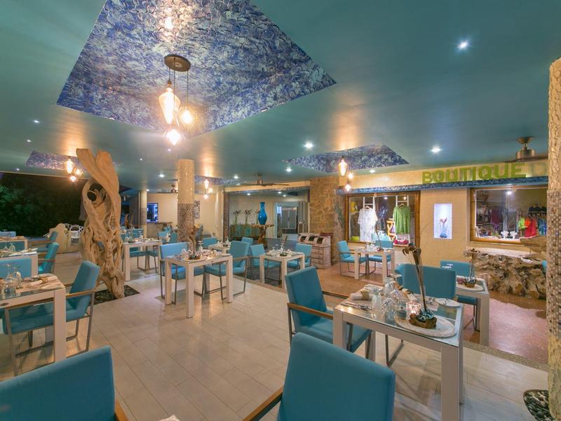Restaurante con sillas azules, madera decorativa, paneles triangulares azules en el techo y ambiente acogedor.