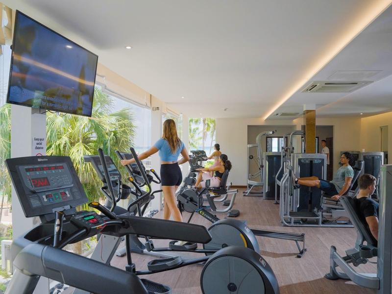 Gimnasio moderno con máquinas cardiovasculares y área de entrenamiento con pesas en un hotel.