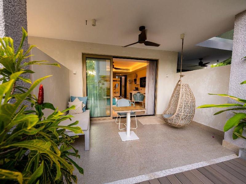 Acogedora terraza con silla colgante, mesa y plantas frente a una puerta de habitación de hotel.