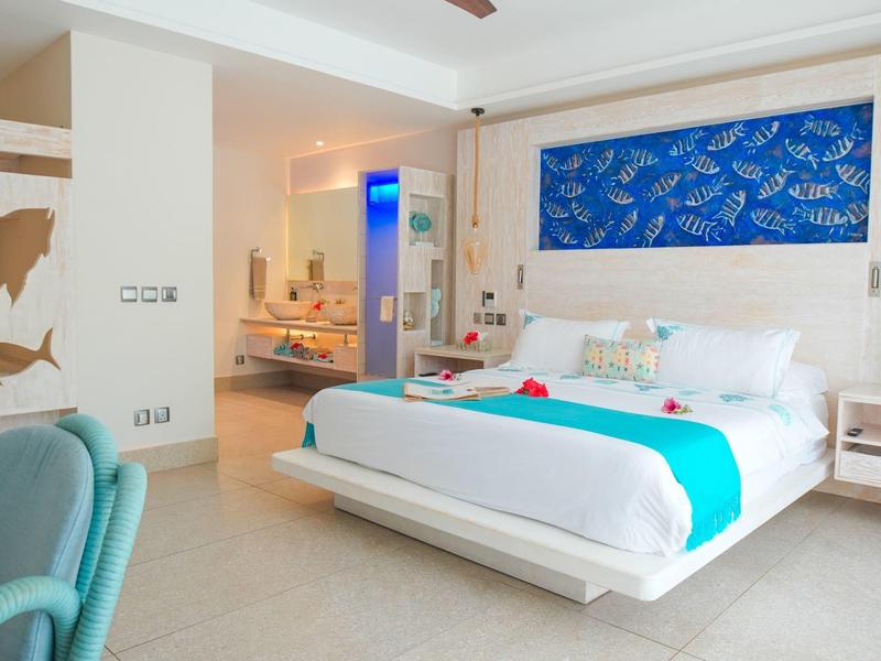 Habitación de hotel luminosa con cama grande, decoración azul y mobiliario moderno y cómodo.