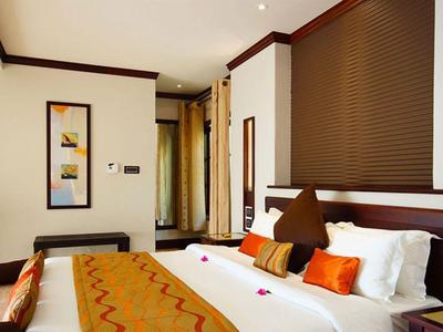 Habitación de hotel acogedora con cama doble, cojines naranjas y cuadro decorativo en la pared.