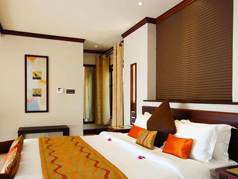 Habitación de hotel acogedora con cama doble, cojines naranjas y cuadro decorativo en la pared.