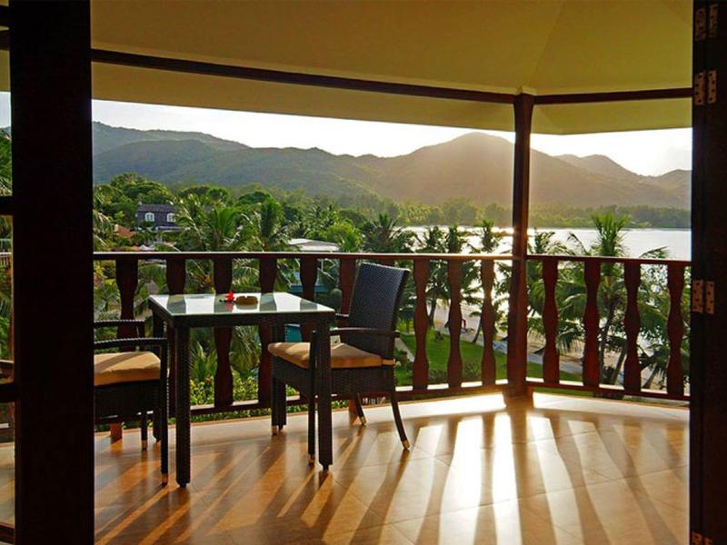 Balkon mit Holzmöbeln und Blick auf Berge und Wasser bei Sonnenuntergang.