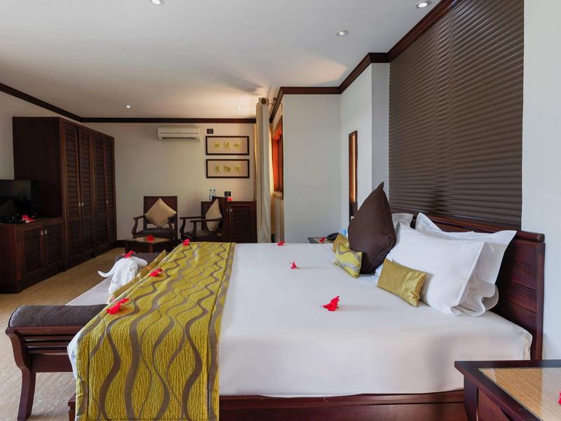 Habitación de hotel moderna con cama grande, manta verde y detalles de madera, decorada de forma acogedora.