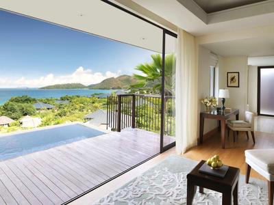 Sala abierta con vista a la terraza, el mar y colinas boscosas bajo un cielo despejado.