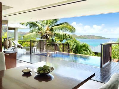 View from a modern terrace with table overlooking a pool, palm trees, and the sea.