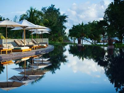 A tranquil pool area with sun loungers and white umbrellas, surrounded by palm trees.