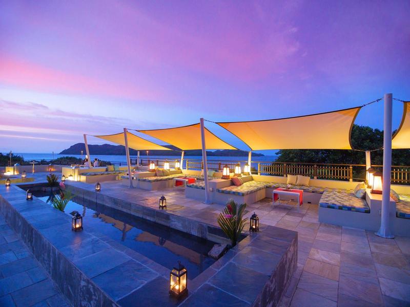 Terraza de hotel moderna con iluminación ambiental y vistas panorámicas al atardecer.