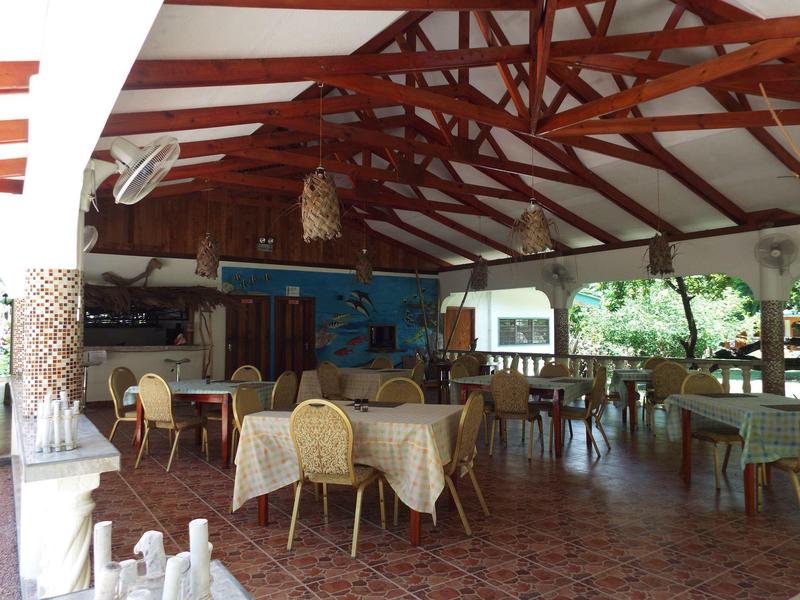 Großer Gastraum mit Holzbalken, verschiedenen Tischen und Stühlen, hellem Innenraum und Blick ins Grüne.