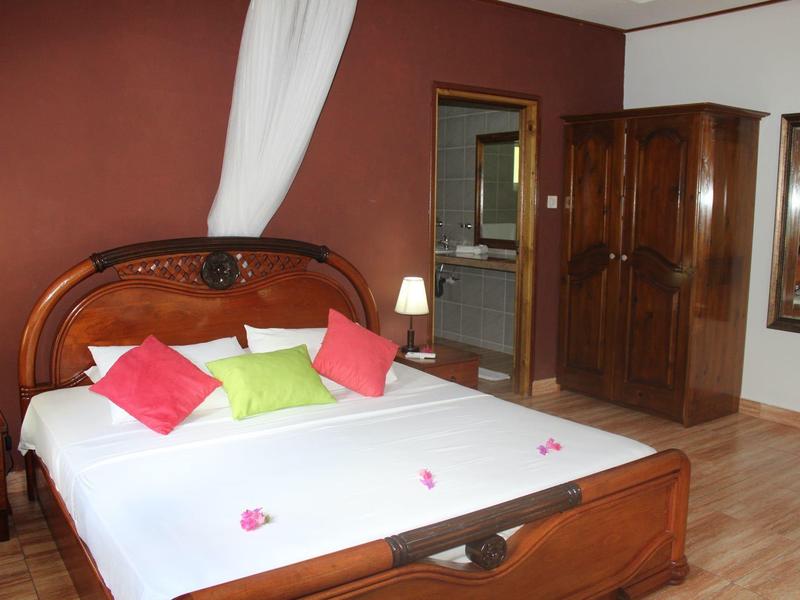 Gemütliches Schlafzimmer mit Holzmöbeln, großem Bett, weißen Wänden und roten sowie grünen Kissen.