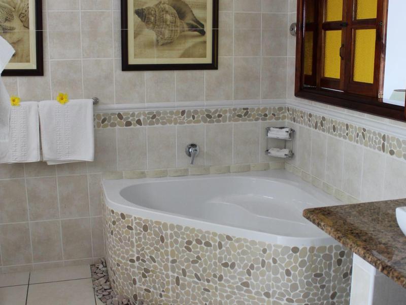 Łazienka z białymi płytkami, wanną mozaikową i oknem w drewnianej ramie.