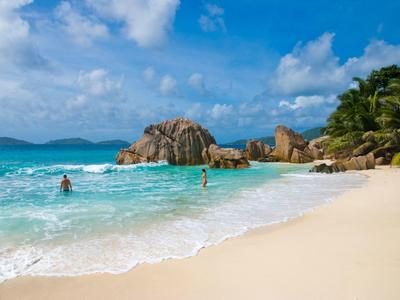 Spiaggia con sabbia bianca, acqua turchese, rocce e palme sotto un cielo sereno.