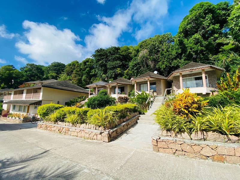 Mehrere weiße Häuser mit brauen Dächern, umgeben von üppigem Grün und blauem Himmel.