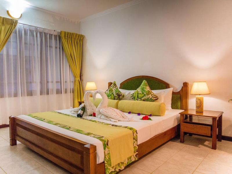 Gemütliches Schlafzimmer mit Holzbett, grüner Bettdecke, Nachttischlampen und gelben Vorhängen.