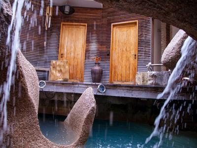 Holztüren und Tontöpfe entlang eines Wasserbeckens mit steinernen Dekorationen und Wasserfall