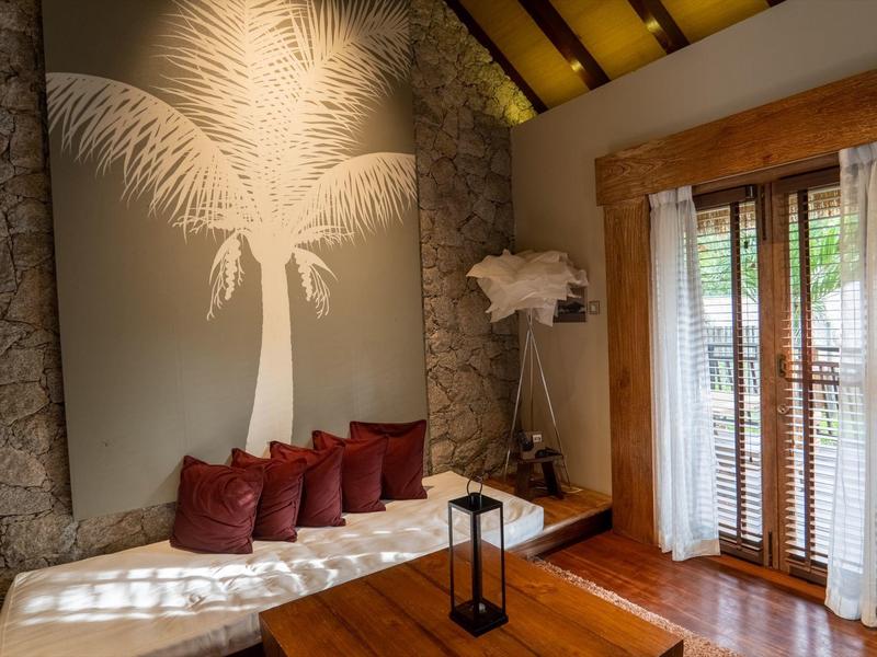 Cozy seating area with palm tree wall decor and wooden tables in a hotel room.