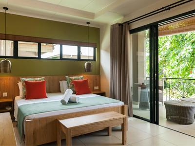 Modernes Hotelzimmer mit Doppelbett, Sitzbank und Balkon mit Gartenblick.