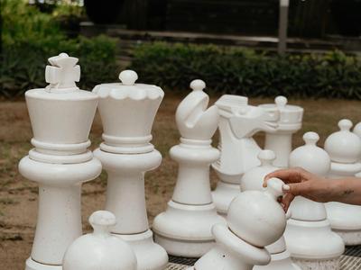 Large outdoor chess game with white pieces on a ground chessboard pattern.