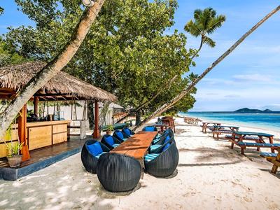 Strandrestaurant mit Tischen, Stühlen und Blick auf das türkisfarbene Meer und den blauen Himmel.