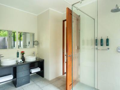 Helles Badezimmer mit großer Dusche und Waschbecken auf schwarzem Unterschrank.