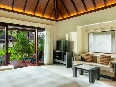 Helle Hotelzimmer mit gemütlicher Sitzecke und Zugang zu einer Holzterrasse mit Gartenblick.