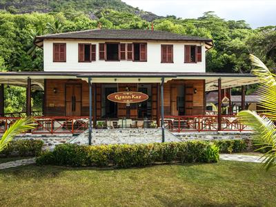 Two-story hotel with wooden facade and outdoor seating area, surrounded by lush greenery.
