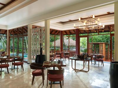 Helles Restaurant mit Holzmöbeln und großen Fenstern mit Blick auf einen Garten.