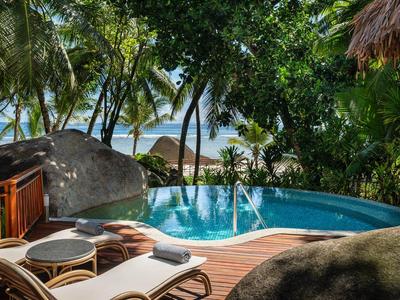 Pool mit Holzdeck und Liegestühlen, umgeben von tropischen Pflanzen und Blick aufs Meer