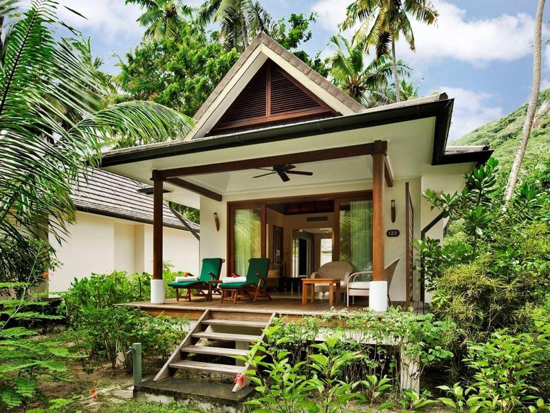 Villa vacacional con veranda y área de estar, rodeada de vegetación tropical exuberante.