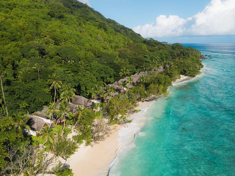 Laderas verdes con chozas en playa de arena blanca junto a mar turquesa claro.