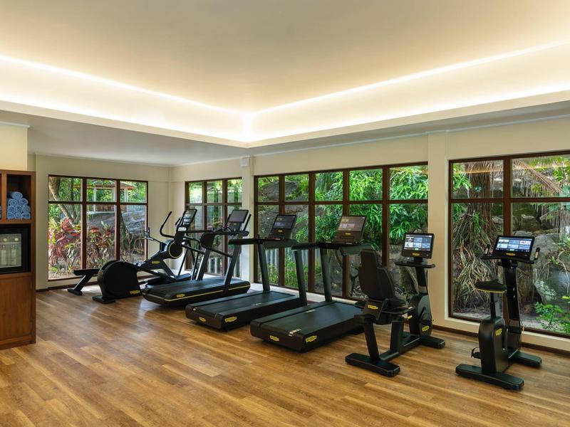 Moderner Fitnessraum mit Laufbändern und Fahrrädern vor großen Fenstern mit Blick ins Grüne.