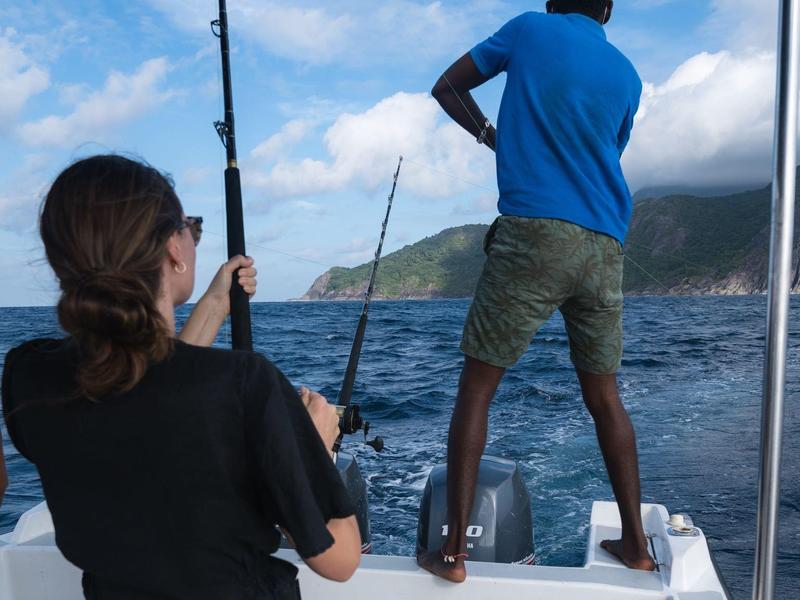 Zwei Personen angeln auf einem Boot mit Blick auf Küste und Himmel.